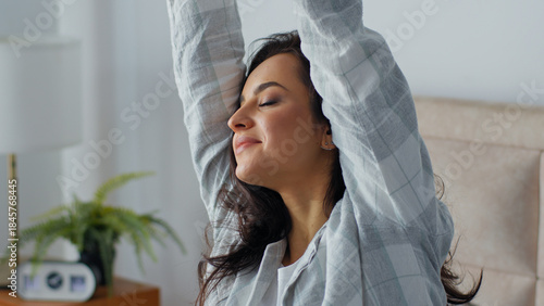 Close up Caucasian woman stretching arms touching neck pain discomfort tension back stretch move head yoga in bed in morning smiling carefree joyful girl female waking up in bedroom lady feeling good