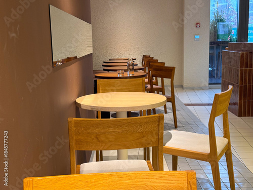 Minimalist cafe interior with empty wooden tables and chairs. Urban quietness, waiting, and everyday public space atmosphere during calm hours between social activity.