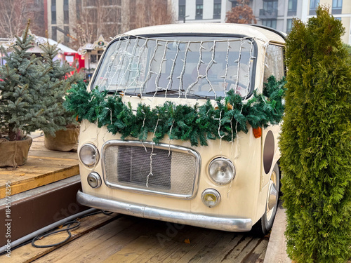 Vintage van decorated with Christmas garland and lights at winter market. Festive urban installation, seasonal decor and holiday atmosphere