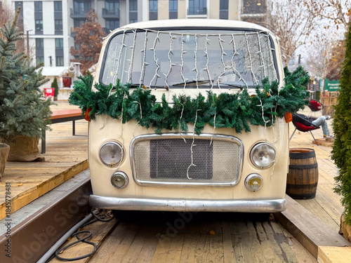 Vintage van decorated with Christmas garland and lights at winter market. Festive urban installation, seasonal decor and holiday atmosphere