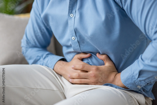 Photos Man clutching his abdomen in visible discomfort from indigestion or cramps, seat