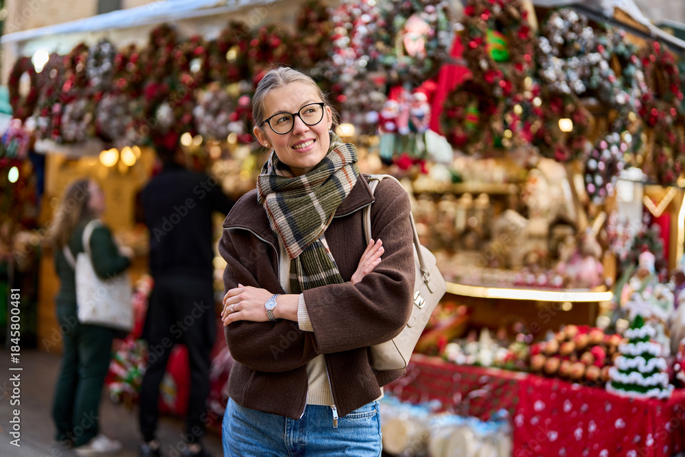 Obraz premium Cheerful young woman looking for New Year decorations in traditional street market