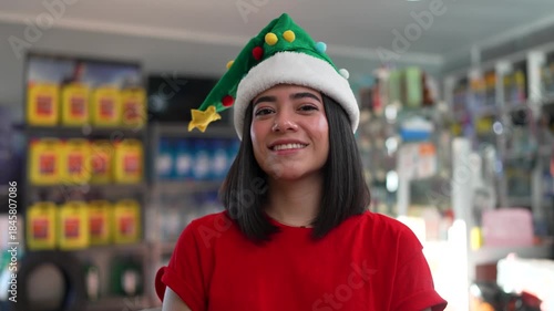 Young latina woman with a christmas hat smiling and gesturing thumbs up in a hardware store