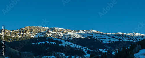 roche parstire dans le beaufortain, une falaise abrupte enneigée avec des sapins et des chalets d'alpage