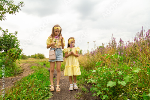 Two girls in an field on a summer day picking flowers.