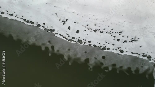 The edge of a river that has defrosted just enough to show the water flowing under the ice and snow layer. The melting snow leaves a unique pattern in the ice on top. 4k, drone, pulling up and away