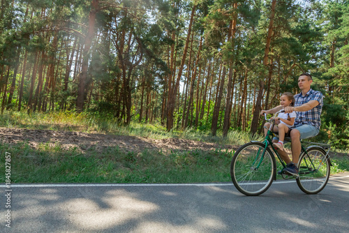 Young father with his little daughter on bicycle in summer sunny forest