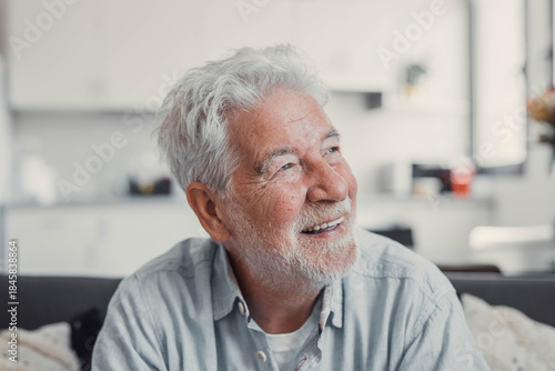 Elderly man sits on a sofa at home looking outside the window. He feels calm and reflective while enjoying a serene moment in his daily life.
