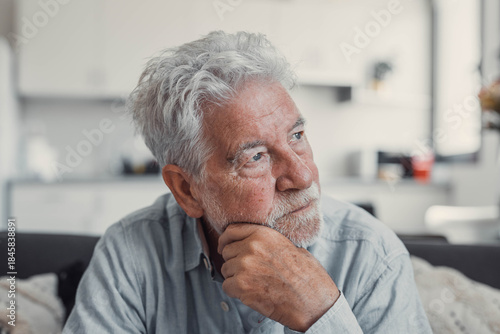 Wallpaper Mural Senior man sits alone on a sofa looking outside with a sad expression. He seems stressed and reflective while dealing with personal concerns at home. Torontodigital.ca