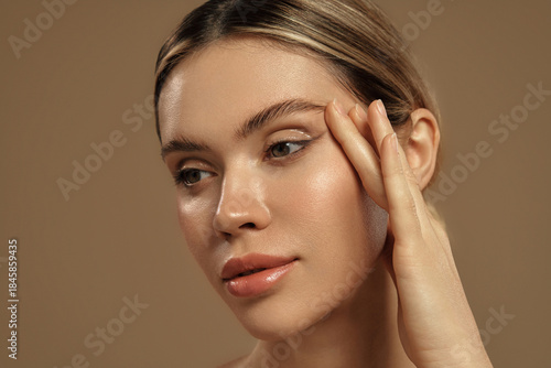 Close-up of a woman touching her face with glowing healthy skin on beige background