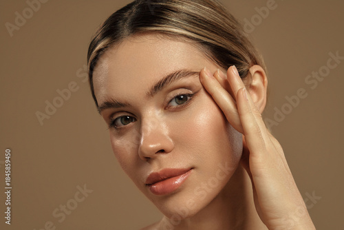 Photography Close-up of a woman touching her face with glowing healthy skin on beige backgro