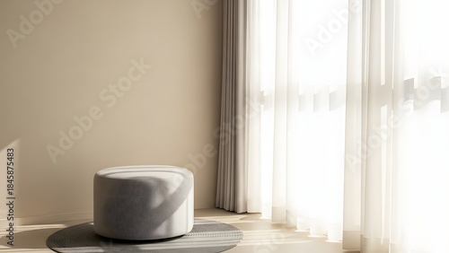 A stylish room with a gray pouf on a rug beside a window with sheer curtains and a beige wall