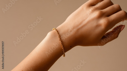 Close-up of a woman’s wrist wearing a gold chain bracelet on a beige background