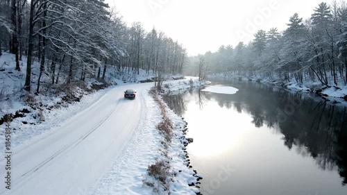 Black Car Driving on Snowy Road Next to Icy River in Winter Forest