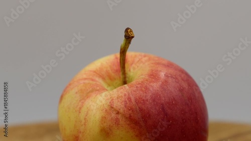 A vibrant close-up shot of a fresh, ripe apple, showcasing its beautiful red and yellow skin with subtle green hues, as it smoothly rotates on a light wooden turntable.