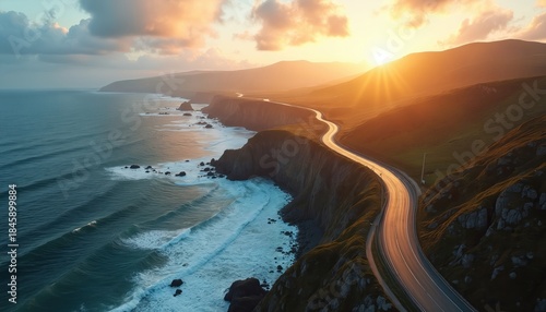 Winding coastal road meets ocean cliffs. Golden hour sun beams onto green hills and blue sea waves crash below. Scenic drive along rugged terrain during warm light.