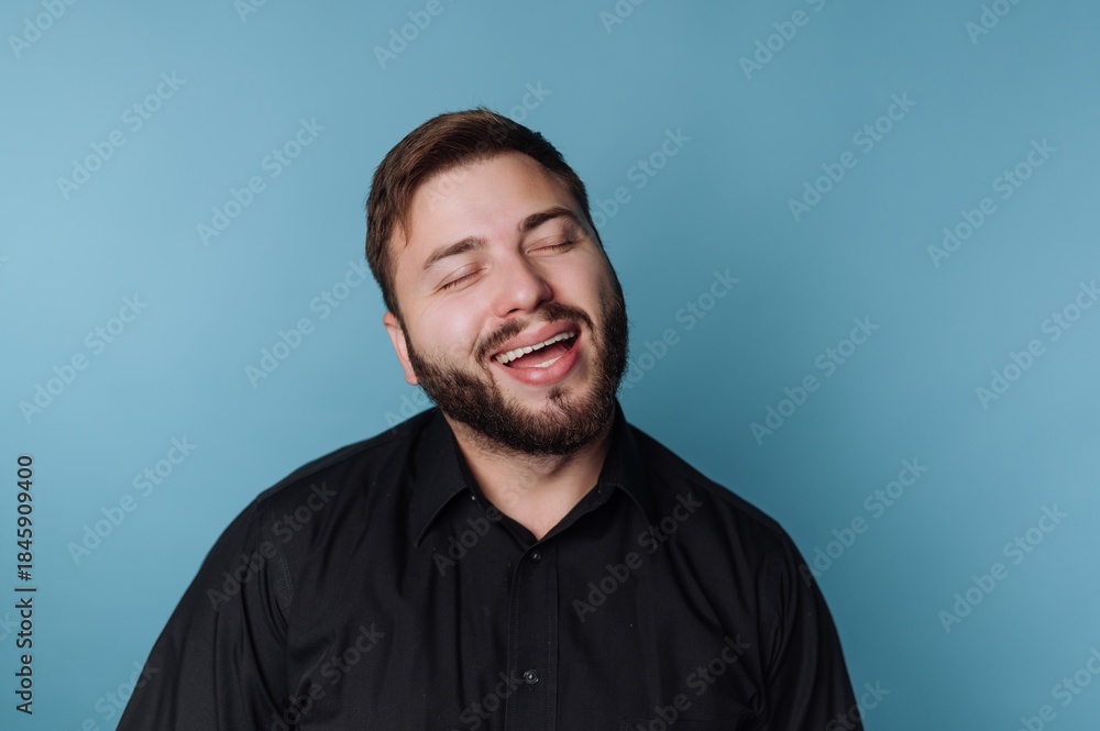 Fototapeta premium Smiling man with a beard wearing a black shirt in front of a blue background during daytime