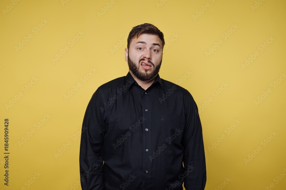Obraz premium Man with beard stands in front of yellow background, making a funny face during a casual moment in a studio setting