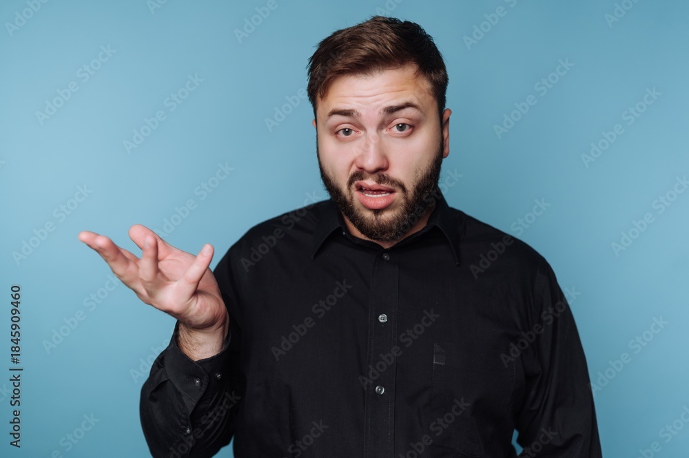 Fototapeta premium Man in black shirt gestures with hand while explaining something in front of a blue background