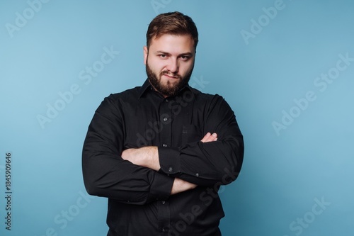 Bild auf Leinwand Man with beard crosses arms and shows expression in front of blue background