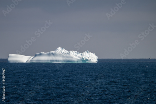 A massive frozen iceberg floats along Iceberg Alley off the coast of Newfoundland. The ice is melting in the deep blue ocean, a sign of global warming and a change in the environment. 