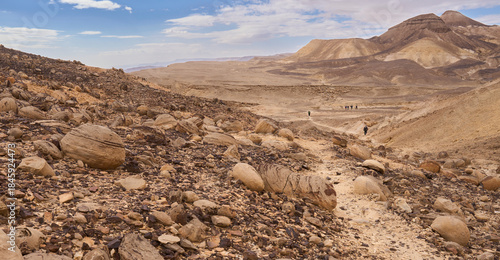 Desert landscape with rounded, potato-shaped limestone nodules called bulbus. A field of round flattened limestones. Hikers in a trail less travelled in a remote part of  the Arava valley.