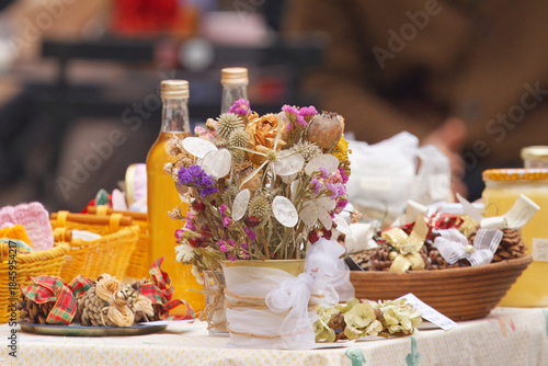 Colorful stall table at Naplavka farmers market in Prague filled with household goods, natural Christmas decorations, dried flowers, honey jars and fruit syrups, capturing festive market atmosphere.