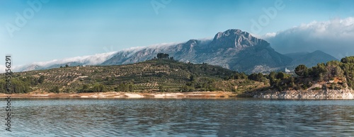 Panoramic view of a tranquil lake with lush green hills and dramatic mountains in South Spain, perfect for travel, nature, and landscape backgrounds or website banners.