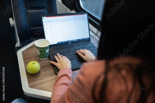 Photos A professional woman works on her laptop in a train, showcasing productivity and focus amid the dynamic environment of travel
