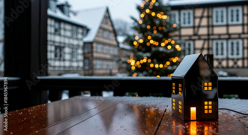 luxury metal miniature house with burning windows on the background of a square with half-timbered houses and a square with a Christmas tree in winter

