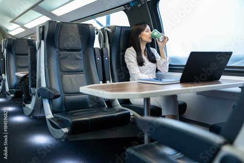 Foto A young woman takes a sip of coffee while seated with her laptop open on a train, reflecting a balance between work and relaxation during her journey
