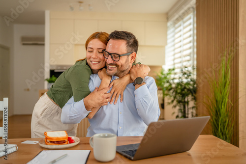 Fotografie Happy couple embracing, working from home with laptop
