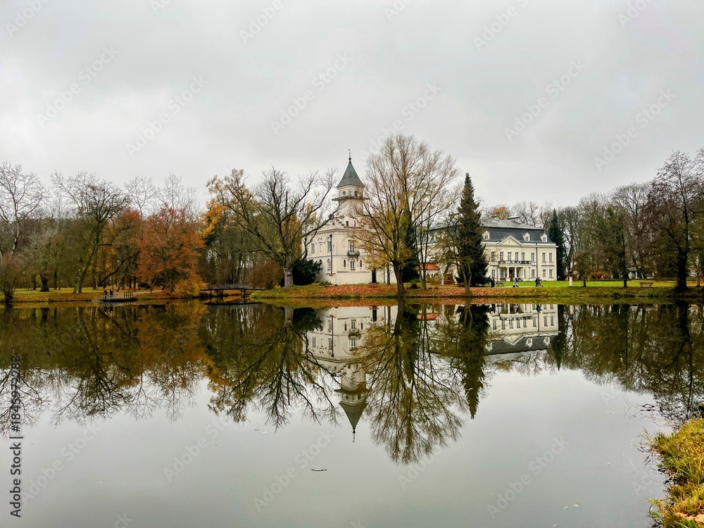 Obraz premium Beautiful autumn view of Radziejowice Palace reflected in a calm lake on a cloudy day. Location: Radziejowice, Poland.