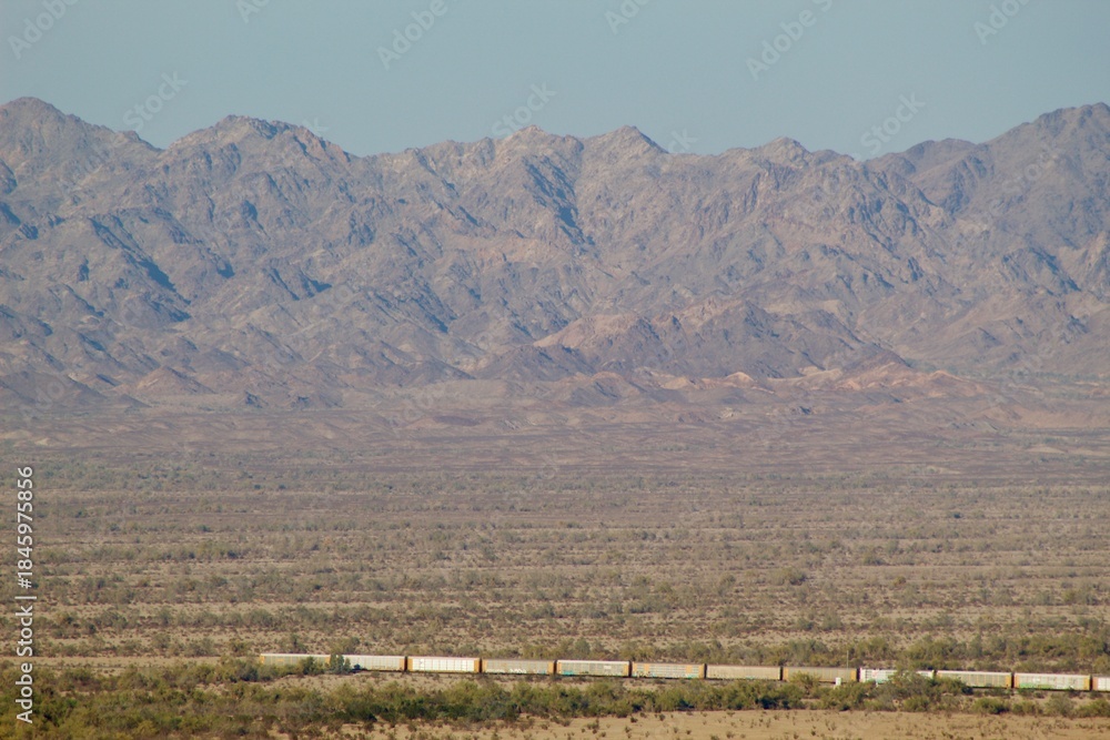 Fototapeta premium Train running through town by Imperial sand dunes with mountainous background in Glamis california