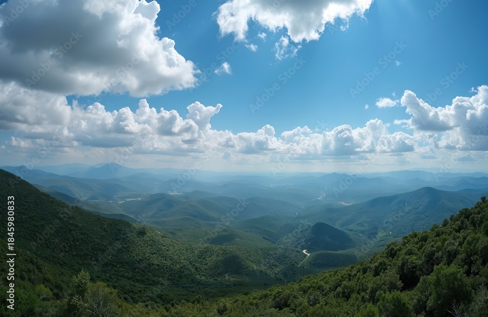 Fototapeta premium Expansive vista of rolling green hills under bright blue sky with fluffy white clouds. Winding river snakes through valley, surrounded by rich vegetation. Natural panorama offers sense of peaceful