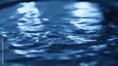 Water drips from a faucet into a sink with blurred lights reflecting in the background 