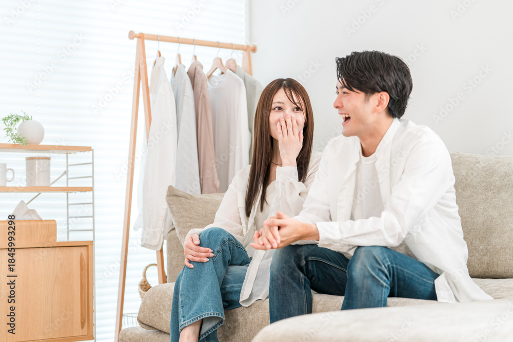 Fototapeta premium Young Asian couple sitting on sofa in living room at home