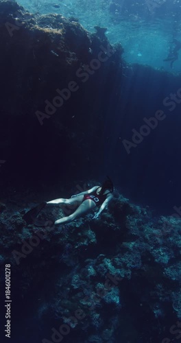 Freediver swims underwater in blue ocean. Woman freediving in near coral reef, vertical rocks