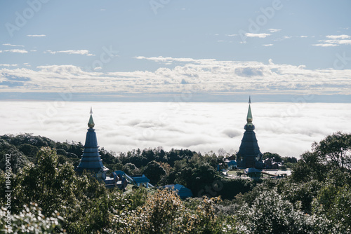 Two pagodas rise above a sea of clouds, framed by lush greenery and a blue sky, creating a serene and majestic landscape.