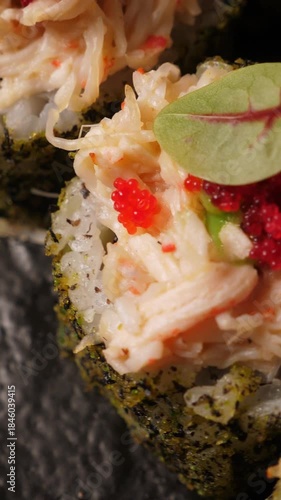 Sushi rolls with tobiko caviar on black platter, closeup. Japanese cuisine . Vertical footage