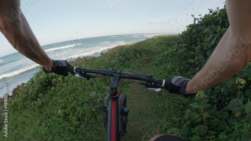 POV. Cyclist rides a mountain bike next to ocean.
