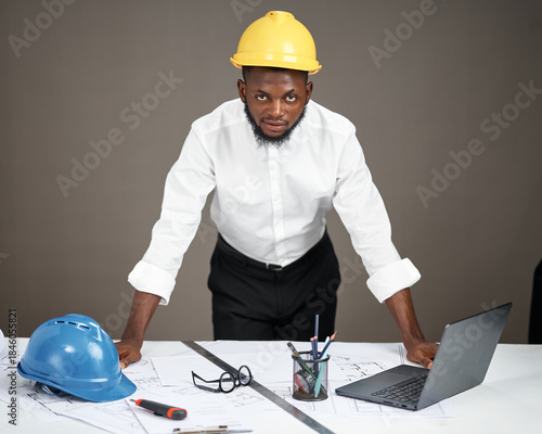 Photos A young Nigerian man wearing a yellow safety helmet and white shirt leans forwar