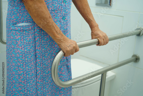 Asian elderly woman patient use toilet support rail in bathroom.