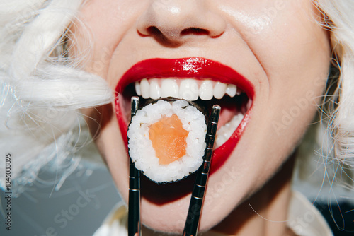 Stylish young woman with bright red lips holding sushi with chopsticks, featuring a joyful expression and vibrant background, perfect for food and lifestyle themes.