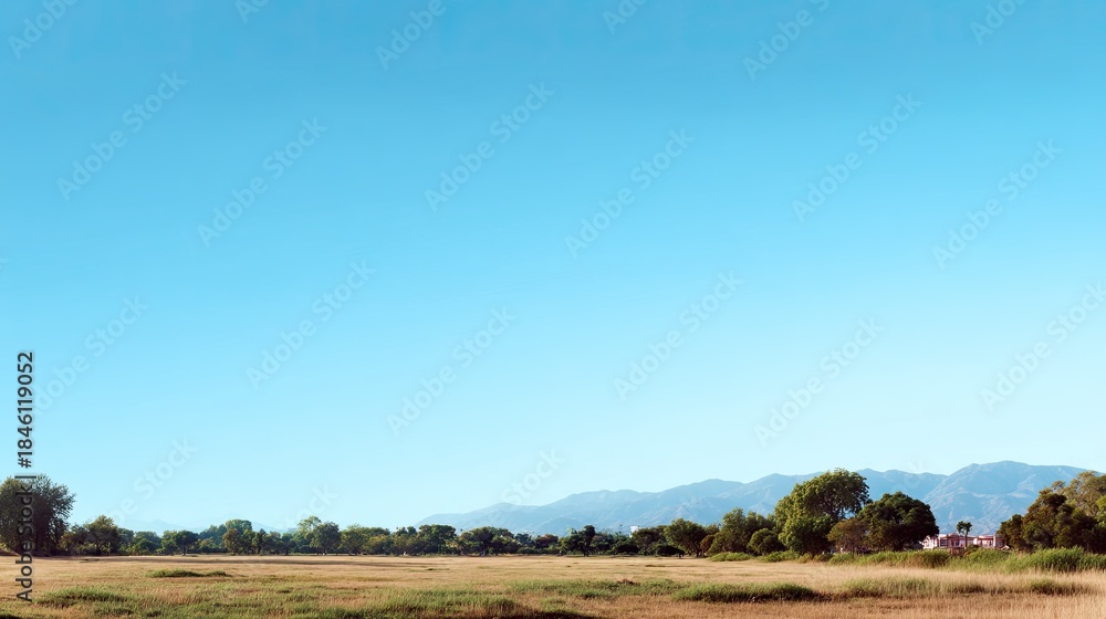 Obraz premium Serene Landscape with Clear Blue Sky Over Green Fields and Distant Mountain Range Under Bright Sunlight in a Tranquil Outdoor Setting
