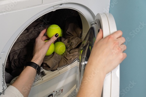 Fotografia A woman places tennis balls into a dryer with clothes, a smart hack for achieving extra fluffiness
