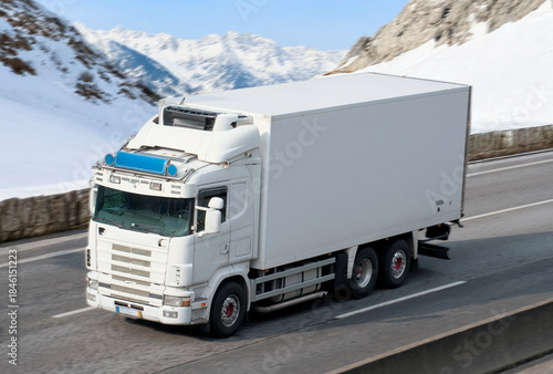 White Box Refrigerator Truck Driving through Snowy Mountain Pass in Winter