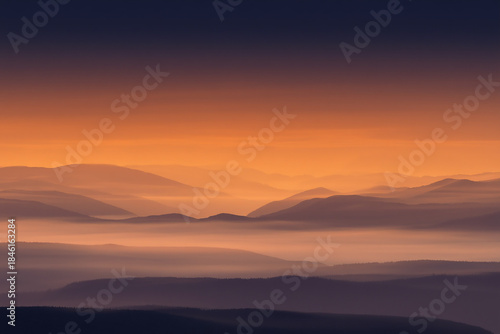 Vibrant sunset over misty mountain landscape with warm orange sky