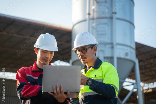 Engineers standing side by side at an industrial facility, carefully checking digital reports on a laptop during routine maintenance planning.