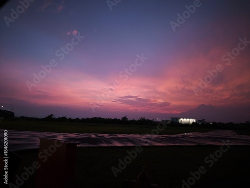 Dramatic purple and pink sunset sky over a dark silhouette landscape and wet ground.
